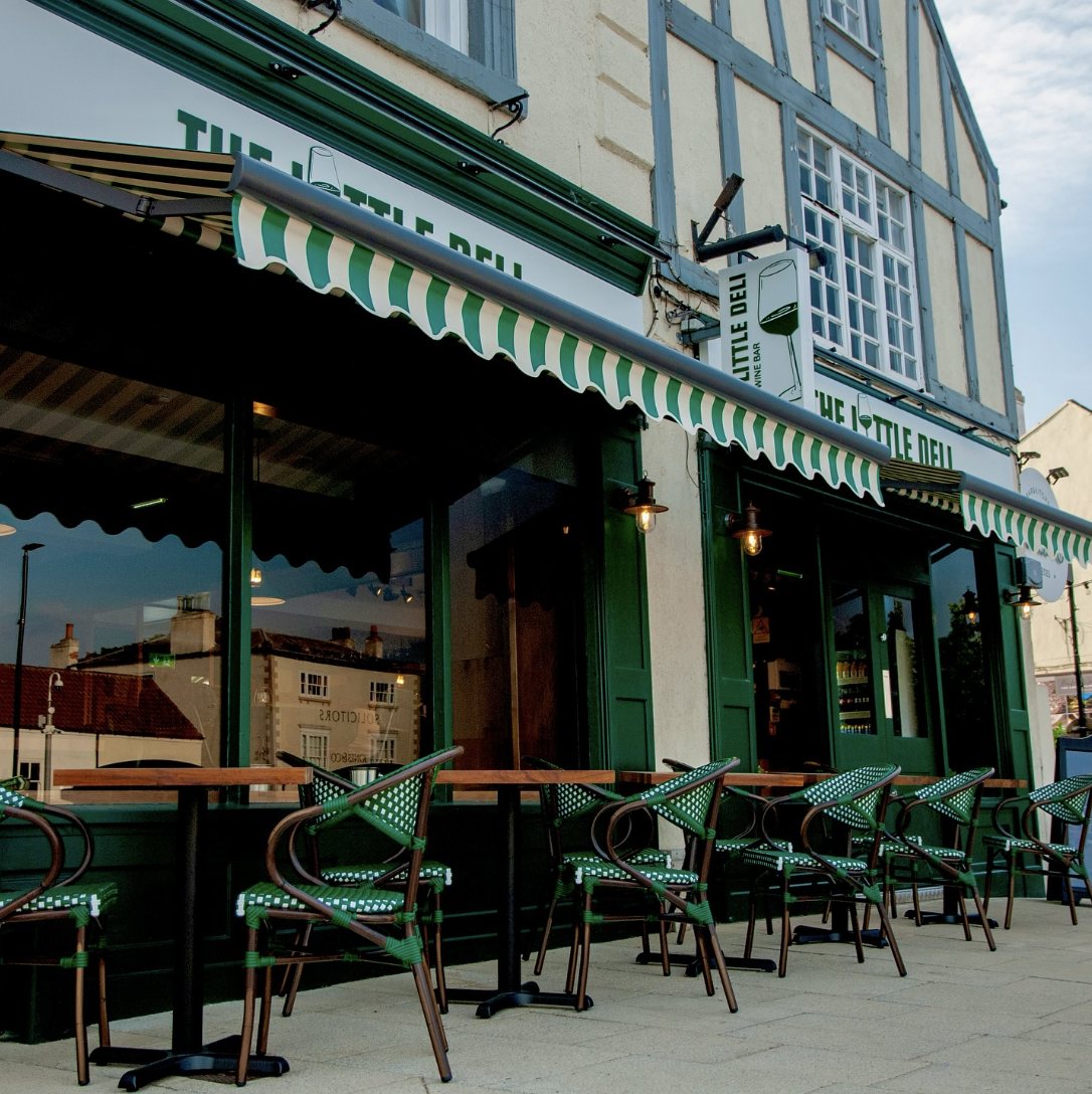 The Little Deli shopfront in Bawtry at dusk, with its green and cream striped awning and tables outside