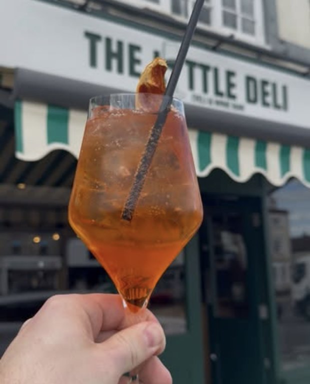 A spritz held up in front of The Little Deli's striped awning